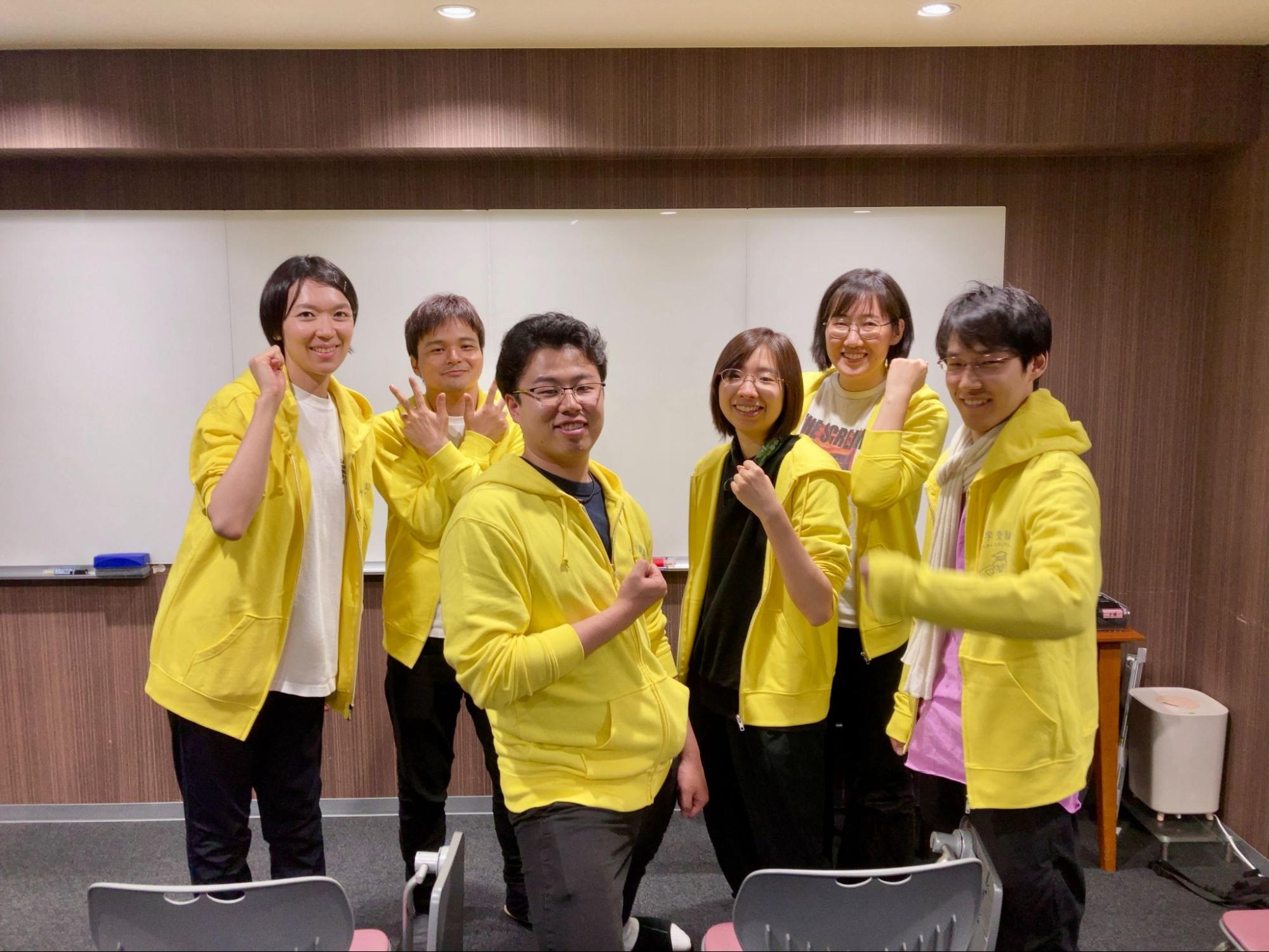塾のスタッフたちが黄色いパーカーを着てポーズをとっている集合写真