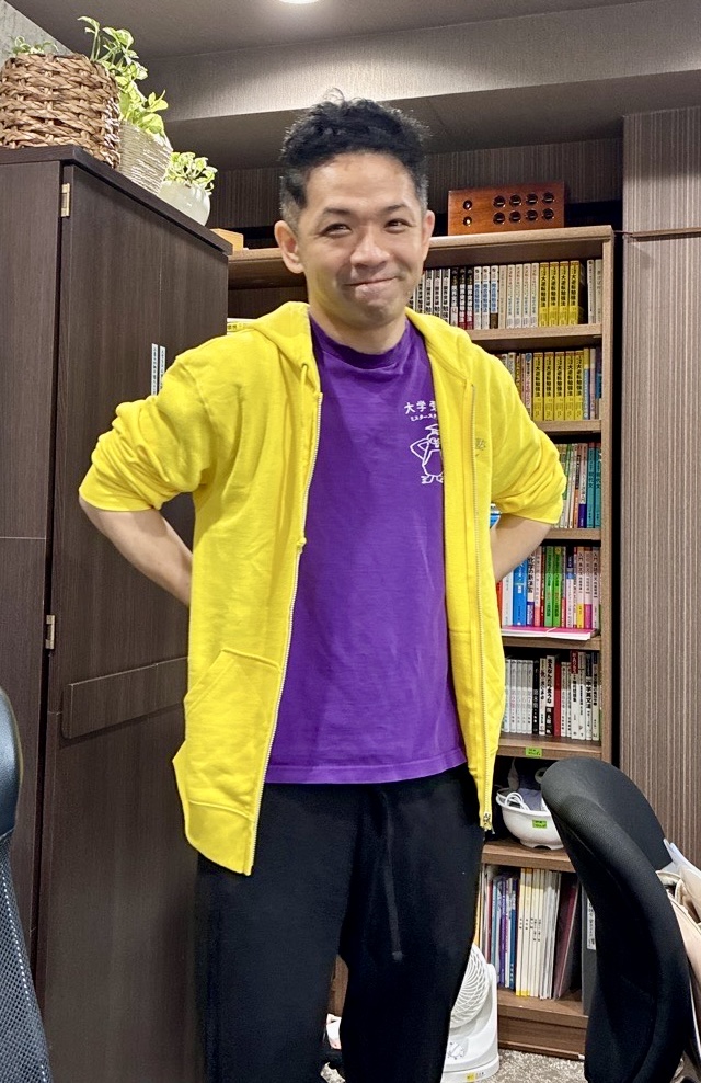 村田塾長が黄色いパーカーを着て照れた表情をしている写真